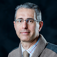 Headshot of a white man with short salt-and-pepper hair and glasses. He is wearing a jacket and matching tie.