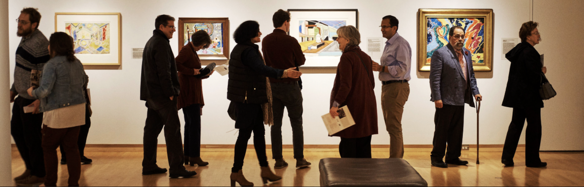 Photo of shadowed people in front of art hung on a wall in a museum