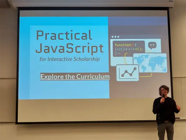 A speaker in front of a powerpoint title slide that says Practical Javascript for Interactive Scholarship