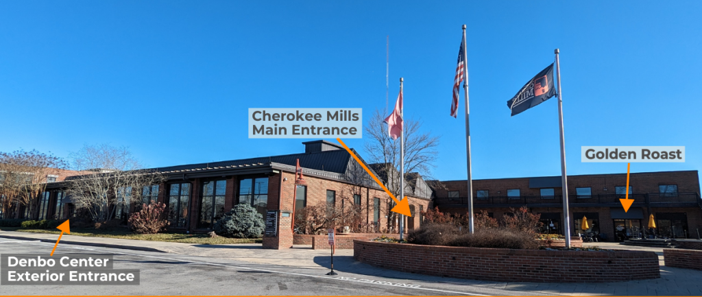 A brick building is below a blue sky. To the right is a courtyard with flags. Parts of the building are labeled.