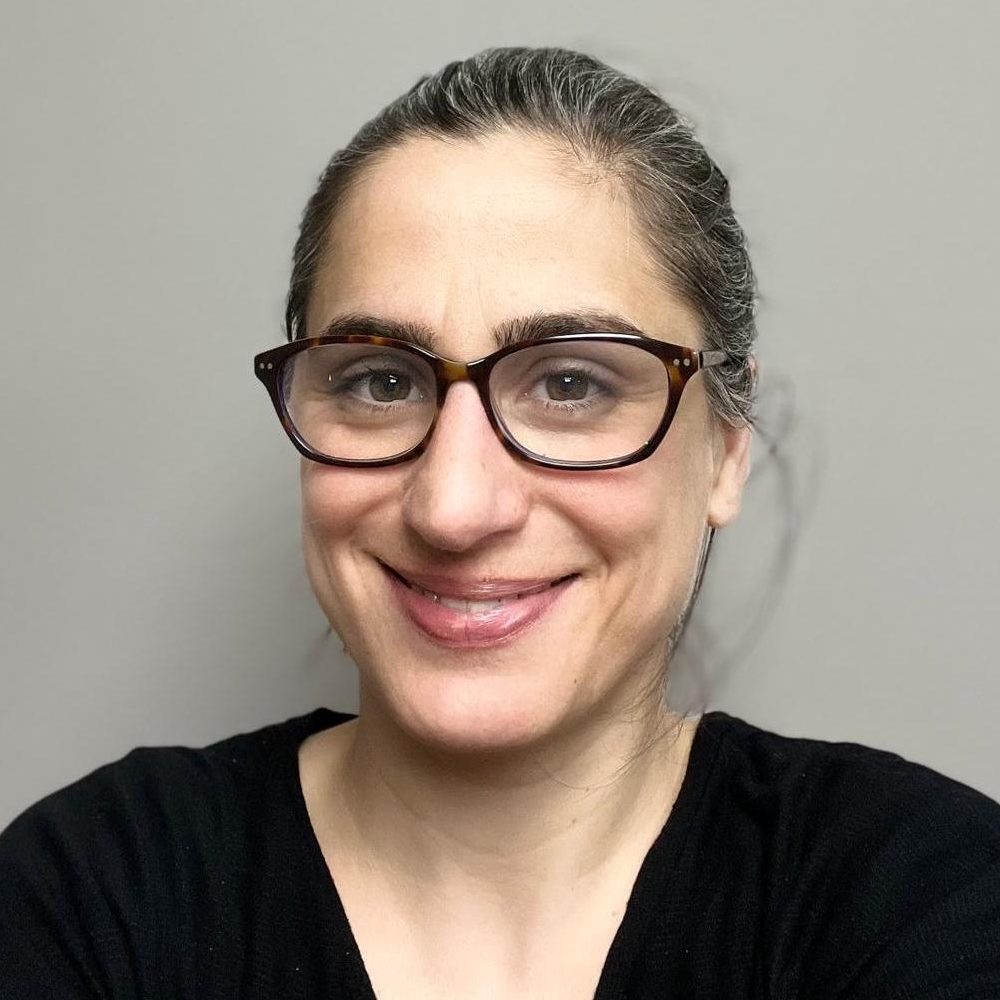 Headshot of a white woman with glasses and a black shirt. Her brown hair is pulled back on her head.