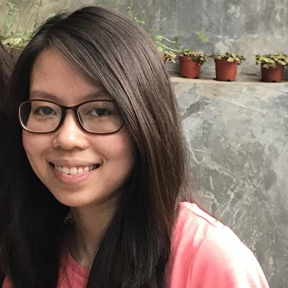 An Asian woman with long hair and glasses smiles at the camera