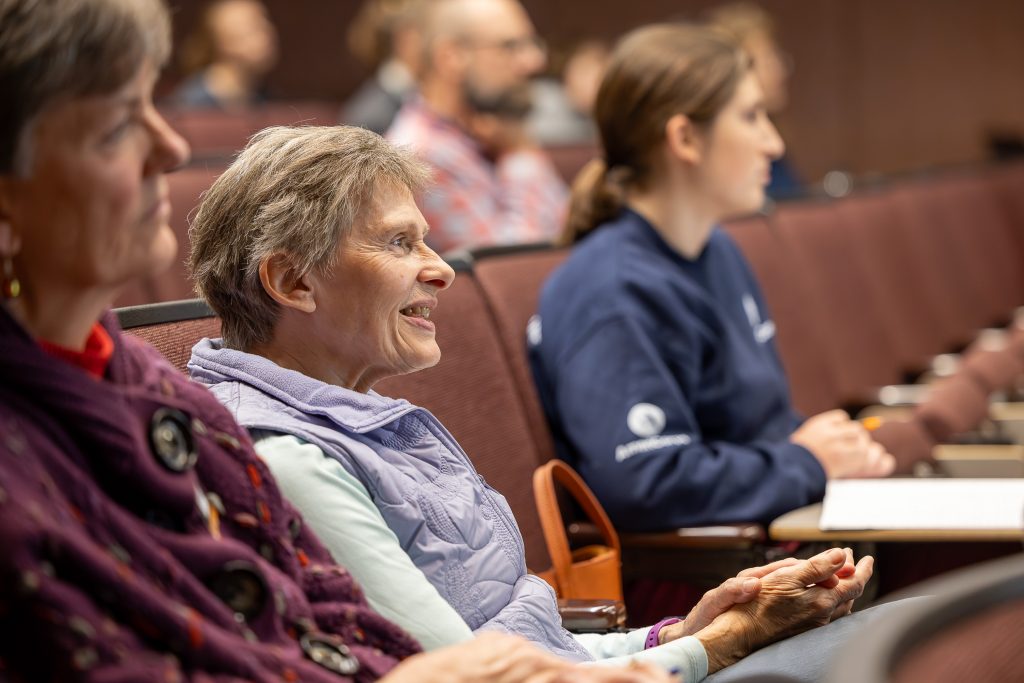 A photo of people in an audience sitting in rows in a lecture hall looking rapt and interested