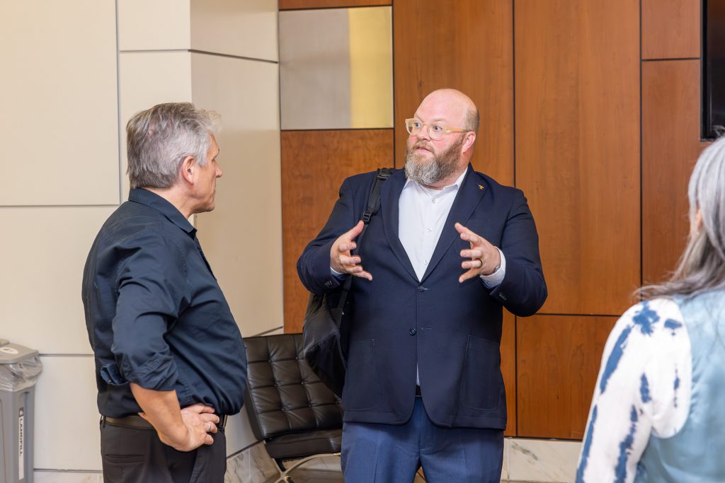 Two white men in navy blue tops stand talking outside a concert hall