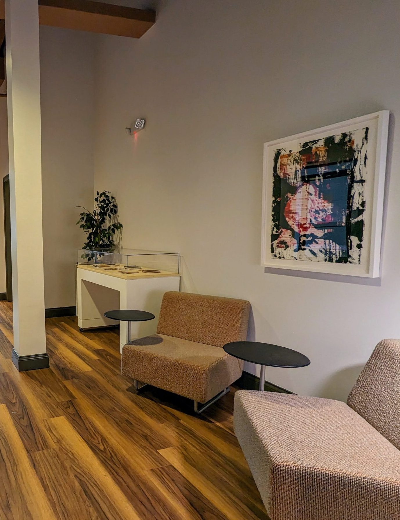 An office reception area contains a couple of soft chairs with small attached desks. Past them is a white display case, and on the wall behind them is an abstract painting of seagulls.