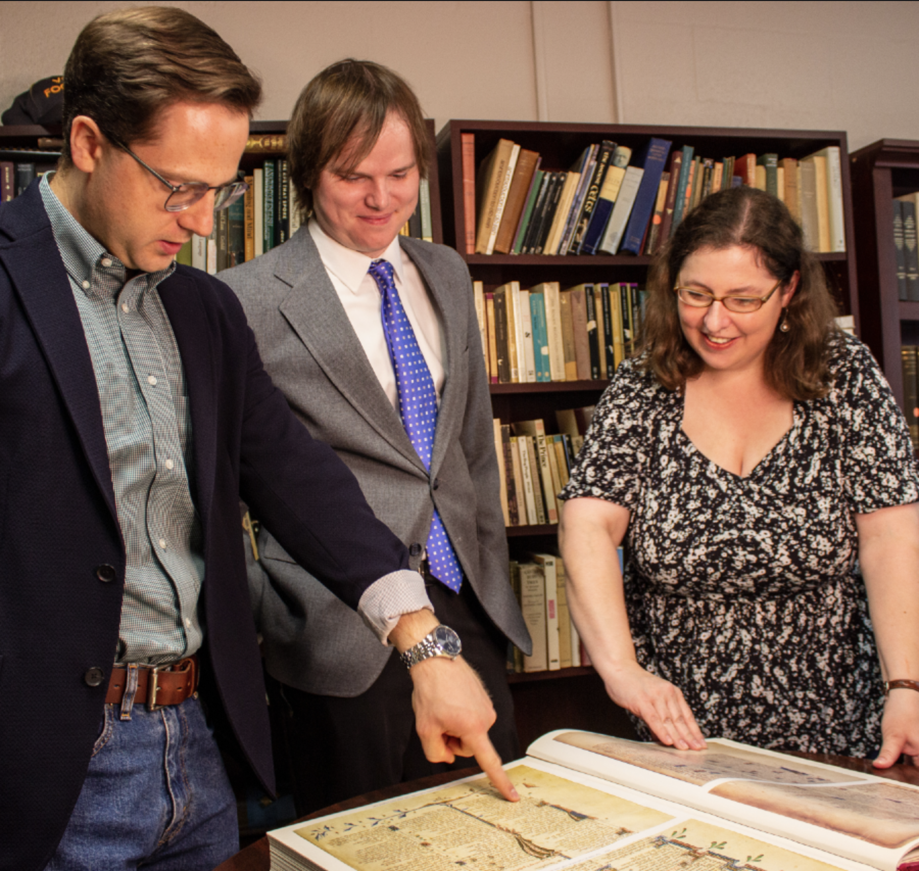 Three people pointing at a large print-out of a manuscript and talking, smiling